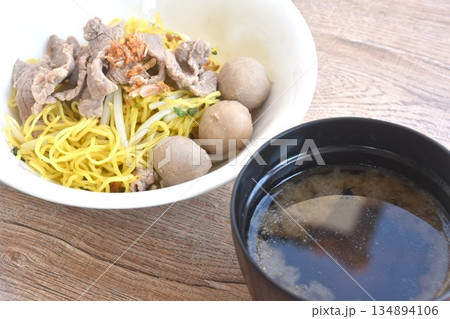 dry boiled Chinese yellow egg noodles with slice beef and meatball topping fried chop garlic on bowl with clear soup cup 134894106