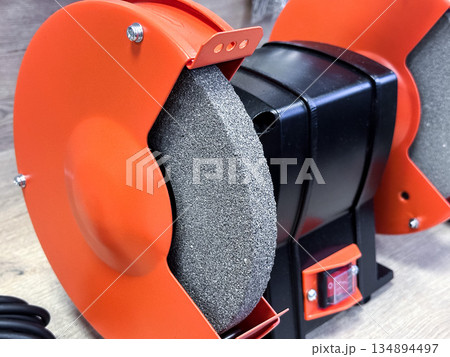 Close-up of an orange bench grinder in a workshop setting. 134894497