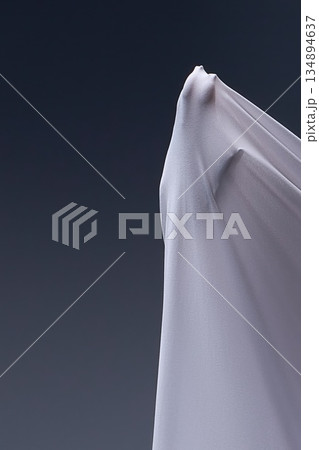 A human hand presses against taut white fabric, creating an abstract, sculptural form against a dark gray background. 134894637
