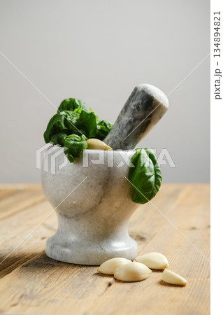 Crushing garlic and basil in a mortar with a pestle on a wooden surface Crushing garlic and basil in a mortar with a pestle on a wooden surface 134894821