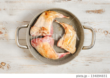Cooking rabbit legs in a metal pot on a wooden table for a meal preparation Cooking rabbit legs in a metal pot on a wooden table for a meal preparation 134894831