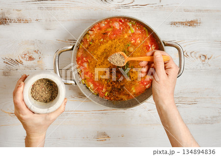 Cooking a mixture of vegetables and spices in a large pot on a wooden table in a kitchen setting Cooking a mixture of vegetables and spices in a large pot on a wooden table in a kitchen setting 134894836