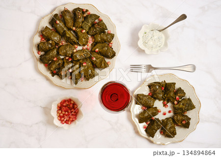 Delicious dishes featuring grape leaves and pomegranate on white marble table 134894864
