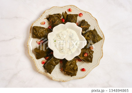 Dish of stuffed grape leaves served with yogurt sauce on a white plate with pomegranate seeds 134894865