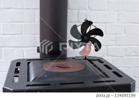 Stove fan heat powered. Black heat stove fan on the top of wood stove to improve heat circulation. Eco-friendly home heating concept 134895199