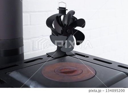 Stove fan heat powered. Black heat stove fan on the top of wood stove to improve heat circulation. Eco-friendly home heating concept Stove fan heat powered. Black heat stove fan on the top of wood stove to improve heat circulation. Eco-friendly home heating concept 134895200