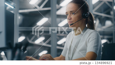 Female Engineer or Technical Support Specialist Wearing Headset and Working Console 134896921