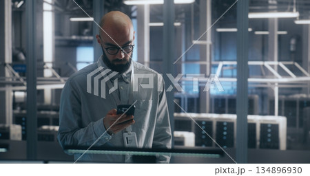 Bearded Male IT Engineer in Glasses Stands and Uses Smartphone to Check Critical Notifications 134896930