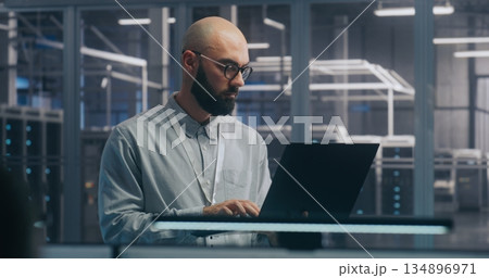 Focused IT Engineer Using Laptop in Server Hall 134896971