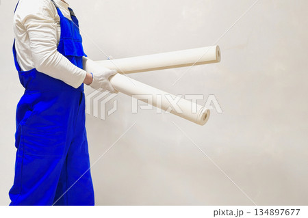 unrecognizable man in a blue jumpsuit is holding two rolls of wallpaper 134897677