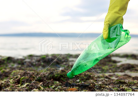 Volunteer picking up a green plastic bottle during beach cleanup, highlighting pollution, waste removal, and environmental protection. 134897764