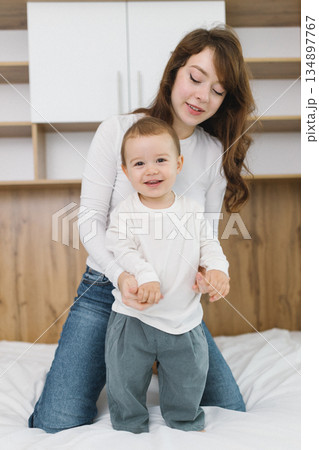 Young mother playing with her baby at home, enjoying a warm and cozy family moment full of tenderness, comfort, natural light, and playful parent-child connection. 134897767