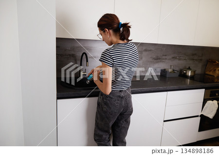 A woman washes dishes in a modern kitchen during the day 134898186