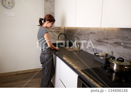 A woman washes a sink in a modern kitchen. A woman washes a sink in a modern kitchen. 134898188
