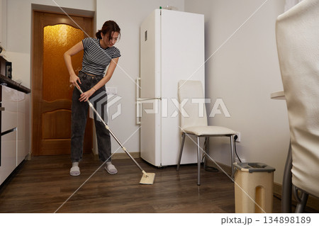 Woman mops floor in modern kitchen during afternoon Woman mops floor in modern kitchen during afternoon 134898189
