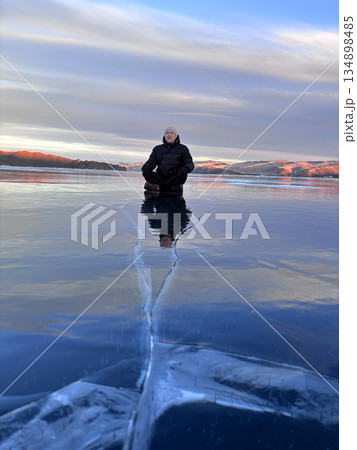 A man walks on the ice of Lake Baikal. A large crack on the transparent ice of the lake. 134898485