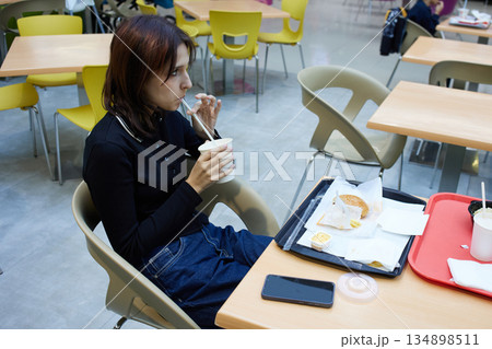 Woman is seated in a food court, sipping a drink from a cup. Woman is seated in a food court, sipping a drink from a cup. 134898511