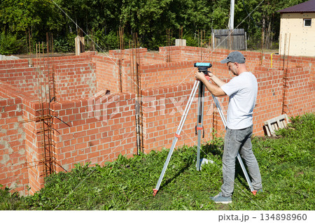 A construction worker checks the height level of the brickwork using a measuring tool on the construction site. A construction worker checks the height level of the brickwork using a measuring tool on the construction site. 134898960