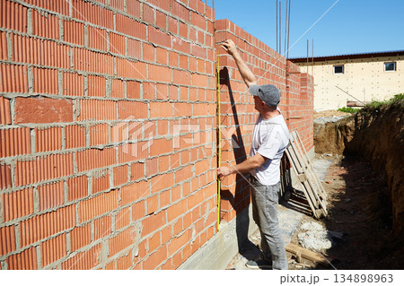 A construction worker is measuring a brick wall at a building site A construction worker is measuring a brick wall at a building site 134898963