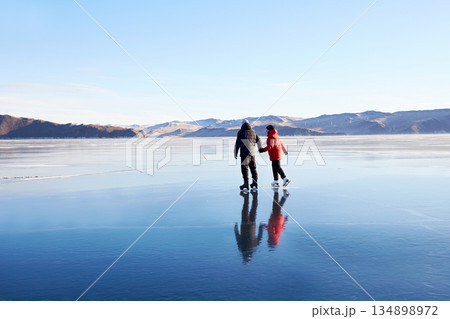 A couple is skating on the frozen Lake Baikal. Transparent ice. A couple is skating on the frozen Lake Baikal. Transparent ice. 134898972