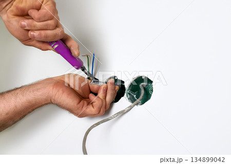 Skilled electrician carefully connects electrical wires in a wall, using a knife tool for precision. Skilled electrician carefully connects electrical wires in a wall, using a knife tool for precision. 134899042