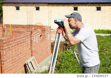 A construction worker checks the height level of the brickwork using a measuring tool on the construction site. A construction worker checks the height level of the brickwork using a measuring tool on the construction site. 134899337