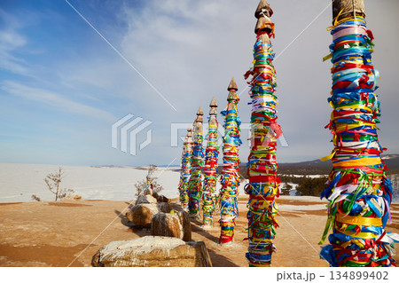 Lake Baikal in winter. Olkhon Island. Wooden ritual pillars with colorful ribbons on cape Burhan or Shamanka rock 134899402