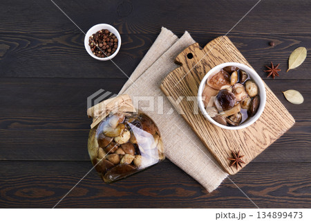 Pickled mushrooms in a glass jar and bowl on dark rustic wooden background. Pickled mushrooms in a glass jar and bowl on dark rustic wooden background. 134899473