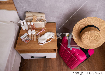 Personal hygiene items, travel cosmetics set on bedside table, bright pink suitcase Personal hygiene items, travel cosmetics set on bedside table, bright pink suitcase 134899474