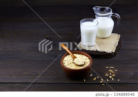 Oatmeal milk and oat flakes on a dark wooden background. Vegetable milk. Oatmeal milk and oat flakes on a dark wooden background. Vegetable milk. 134899548