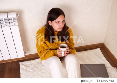 A sad girl in warm clothes with a cup of hot tea in her hands 134899748