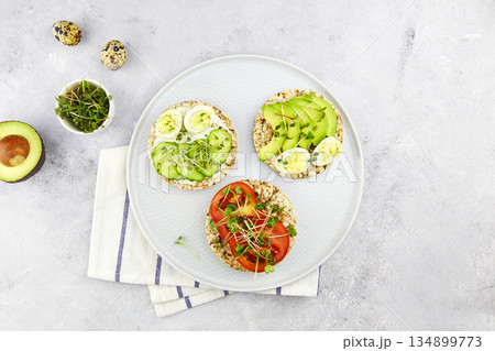 Three toasts with egg, avocado, micro greens, cucumbers and tomatoes. Three toasts with egg, avocado, micro greens, cucumbers and tomatoes. 134899773