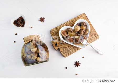 Pickled mushrooms in a glass jar and bowl on white wooden background. Pickled mushrooms in a glass jar and bowl on white wooden background. 134899782
