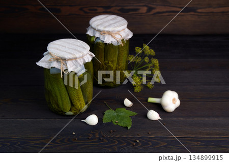 Pickled cucumbers in a jars on a dark wooden background. 134899915