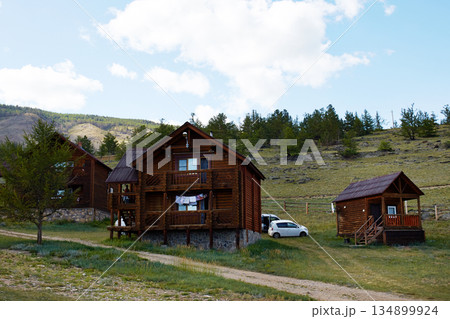 Rustic wooden cabins stand against a backdrop of hills and trees, creating a peaceful setting. 134899924
