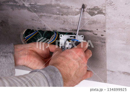 Electrician installing electrical outlets in a wall made of porcelain tiles. Electrician installing electrical outlets in a wall made of porcelain tiles. 134899925