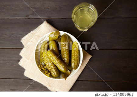 Marinated cucumbers and pickled juice on a dark wooden background. Marinated cucumbers and pickled juice on a dark wooden background. 134899968