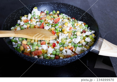 Fresh vegetables with rice, including peas, corn and sweet peppers, are fried in a frying pan. Fresh vegetables with rice, including peas, corn and sweet peppers, are fried in a frying pan. 134899970