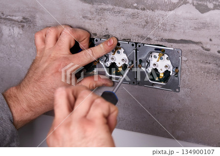 A worker installs an electrical outlet into a wall using a screwdriver 134900107