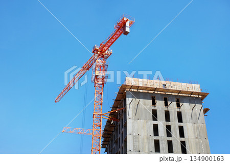 A crane on a construction site against a blue sky with clouds. A crane on a construction site against a blue sky with clouds. 134900163