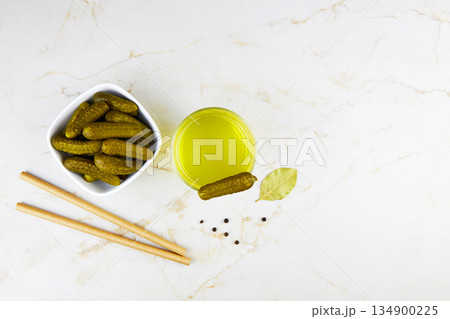 Pickled cucumbers in a bowl and pickle juice in glass on a light background. Pickled cucumbers in a bowl and pickle juice in glass on a light background. 134900225