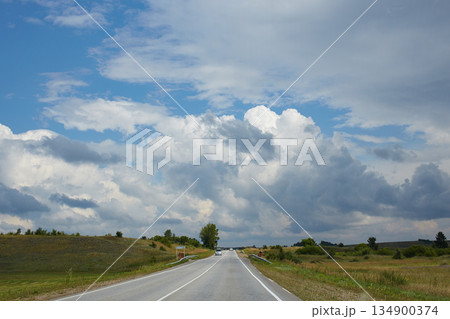Cars drive along a paved road surrounded by vast meadows and hills. 134900374