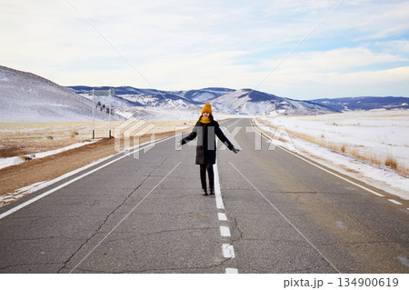 A girl traveler walks on an empty asphalt road to Lake Baikal on a winter day A girl traveler walks on an empty asphalt road to Lake Baikal on a winter day 134900619