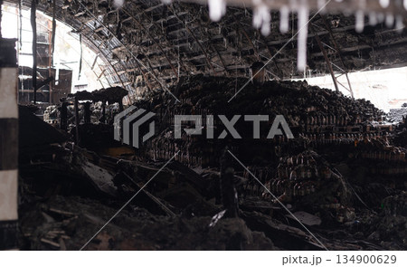 Burned warehouse interior with collapsed roof and stacks of melted plastic bottles, depicting industrial fire damage 134900629