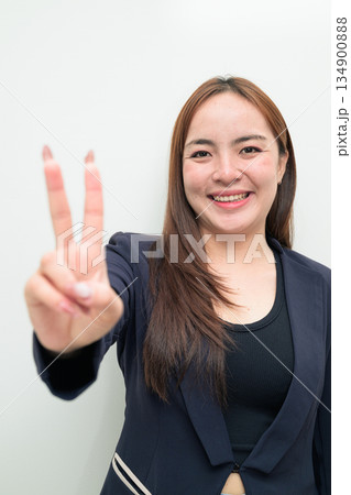 Portrait of a young Asian businesswoman against white background making peace sign gesture 134900888