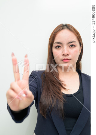 Portrait of a young Asian businesswoman against white background making peace sign gesture 134900889