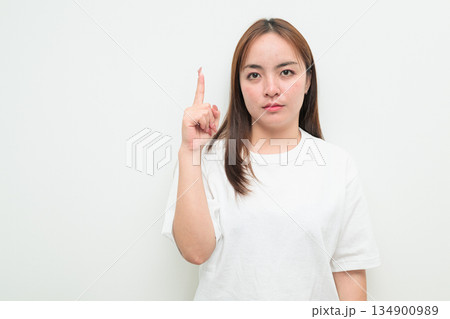 Portrait of a young Asian woman against white background pointing finger Portrait of a young Asian woman against white background pointing finger 134900989