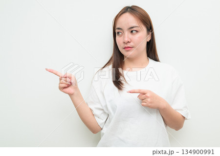 Portrait of a young Asian woman against white background pointing finger Portrait of a young Asian woman against white background pointing finger 134900991