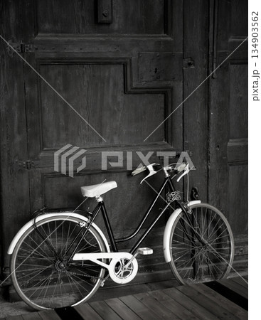 Aged vintage black bicycle, big wooden door, black and white 134903562