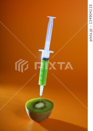Injection with syringe to a green kiwi fruit over orange background Injection with syringe to a green kiwi fruit over orange background 134904218